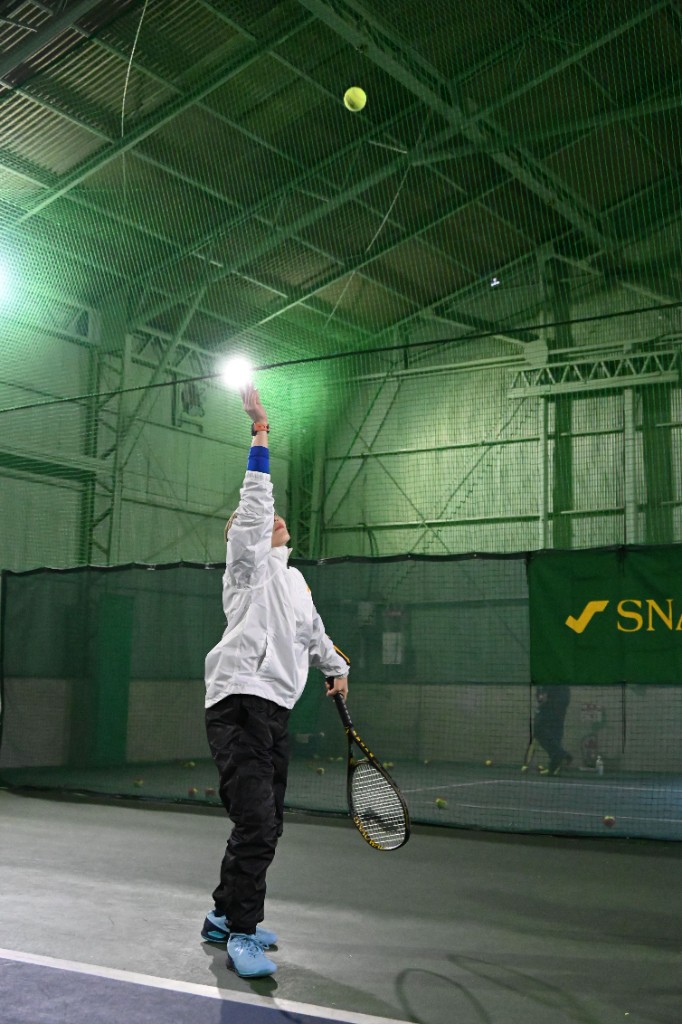 インドアコートでサーブの構えをするテニスプレイヤーとスノワートのバナー